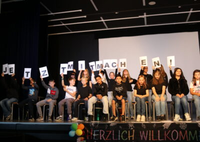 Schüler:innen stehen auf der Bühne und halten den Satz "Das kann ich auch" in die Höhe